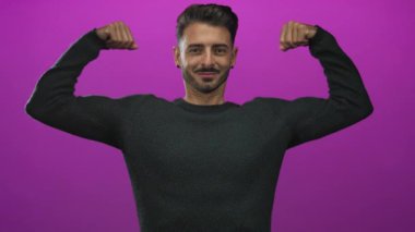 Genç İspanyol adam stüdyoda canlı mor bir duvara karşı iki kolunu esnetiyor; kendine güveni güçlü..