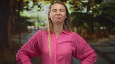 Pembe tişörtlü genç beyaz kadın yeşil bir parkta gözleri kapalı duruyor. Etrafı bulanık doğa ile çevrili duygular ve derin düşüncelere dalmış..