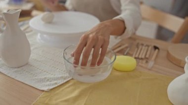 Stüdyoda çömlekçi çarkında kil şekillendiren elleri olan önlük giyen genç bir kadın; yaratıcılık odaklı zanaat sakinliği.