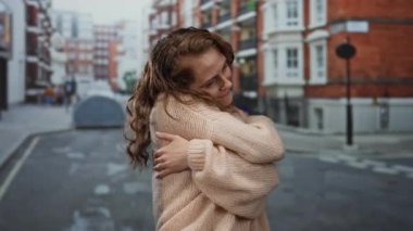 Şehir caddesinde mutlu bir şekilde gülümseyen genç bir kadın. Kolları rahat bir süvetere sarılmış, arka planda bulanık binalar olan bir şehir ortamında neşe ve kendine olan sevgiyi somutlaştırıyor..