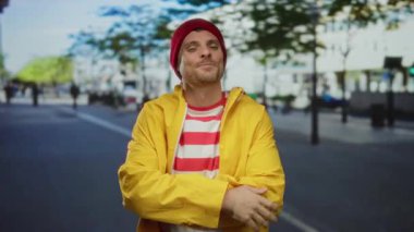 Sarı ceketli ve kırmızı çizgili gömlekli genç adam şehir arka planında barış işareti yapıyor..