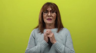 Minnettarlığını kapalı gözler ve ellerle ifade eden bir kadın canlı sarı bir arka plana yapışmış, İspanyol kökenli bir duygu ve pozitiflik sergiliyor..