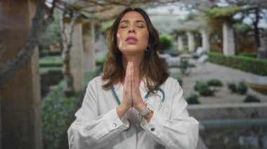 Kadın doktor steteskop ve odaklanmış ifade ile açık hava parkında meditasyon yapıyor. Huzurlu bir ortamda farkındalığı ve huzuru somutlaştırıyor..