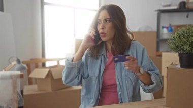 Yeni evde elinde kutular olan bir kredi kartıyla telefonla konuşan bir kadın içeride finans işleriyle meşgul bir İspanyol kadını öneriyor..