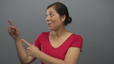 Gri stüdyo ortamında dinamik duruşu olan ve çerçevenin dışına doğru gülümseyen bir kadın. Sürpriz..