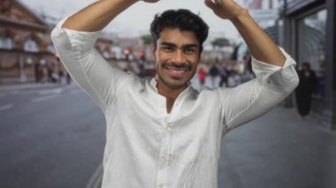 Beyaz gömlekli İspanyol adam kollarını yukarı kaldırıyor ve sokakta dostça bir ifadeyle gülümsüyor; iyimserlik.