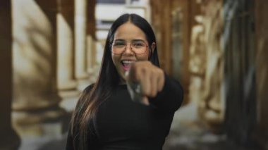 Eski kasabada gülümseyen bir kadın, kameraya karşı dostça bir jest sergiliyor. Tarihi mimarisi ve parlak gözlükleriyle açık havada ifadesini geliştiriyor..