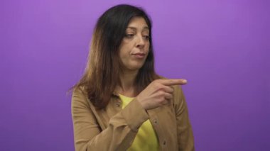 İspanyol kadın tarafsız ifadeyle mor stüdyo duvarına başıyla işaret ediyor, şüphecilik....