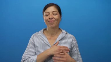 Orta yaşlı bir kadın mavi duvarlı stüdyoda kalp krizi geçirmek için göğüs göğüse baskı yapıyor..