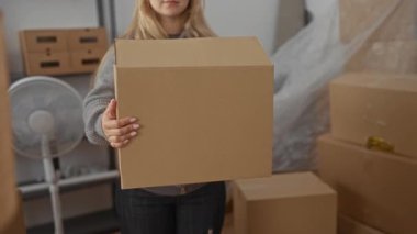 Yeni apartman dairesinde kutuları açan kadın, elinde karton paketle gülümsüyor ve içeriyi düzenliyor..