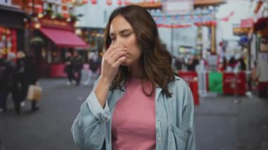 Meşgul şehir caddesinde pembe gömlekli bir kadın endişeli bir ifadeyle burnunu kapatırken kalabalık parlak kentsel arka planla süslü kemer yolunun altından geçiyor.