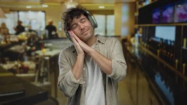 Kulaklık takan bir adam, hareketli bir bar ortamında uyur. İçerideki hareketli ortamda rahatlık ve rahatlık yayar..