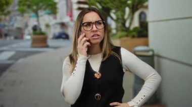 Dışarıda telefonla konuşan, ağaçlarla kaplı sokaklarda duygularını ifade eden, şehir yaşam tarzını ve iletişimini gösteren bir kadın..