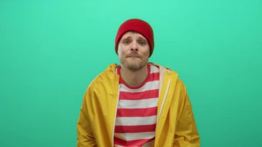 Kırmızı bereli ve sarı ceketli genç adam canlı yeşil bir arka plana karşı poz veriyor. Çekici ve neşeli bir ifade takınıyor..