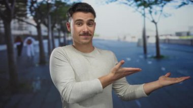 Latin kökenli genç bir adam şehir dışındaki bir sokak manzarasına el uzatıyor. Arka planda ağaçlar olan bir şehir manzarası sunuyor. Geniş ve misafirperver bir ortam yaratıyor..