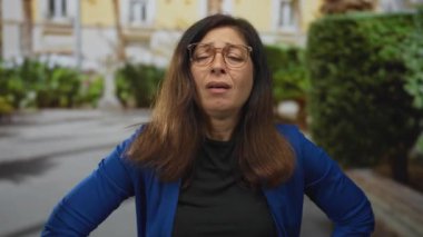 Orta yaşlı İspanyol kadın güneşli şehir sokağında alnı ağrılı, stres yorgunluğu baş ağrısı.