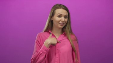 Pembe tişörtlü genç bir kadın canlı pembe bir arkaplan üzerinde kendini küçümseyici bir ifadeyle gösteriyor, izole edilmiş ve eliyle 