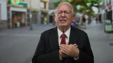 Takım elbiseli kıdemli bir adam sokakta dikiliyor. Duygusal görünüyor. Elleri kalbinin üzerinde, bulanık bir kentsel çevre ile çevrili..