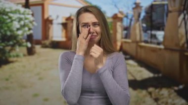 Parkta yüzü koyun ağlayan kadın, doğal ortamda ayakta duran, güneşli koşullar altında günlük giysiler giyen, doğada duygusal sıkıntı ya da neşe olduğunu öne süren kadın..