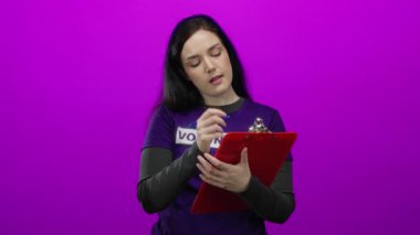 Gönüllü tişört giyen esmer kadın kırmızı bir pano ve kalem tutan canlı pembe bir arka plana karşı duruyor, çekici ve düşünceli bir ifade sunuyor..