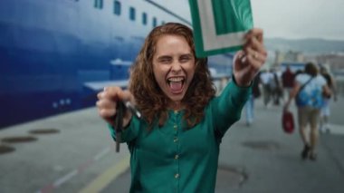 Genç bir kadın heyecanlı bir şekilde elinde anahtar ve deniz kıyısında bir kart tutuyordu. Bulutlu bir günde arka planda bir yolcu gemisi vardı..