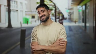 Şehirdeki bir caddede güvenle sırıtan İspanyol bir adam, açık hava ortamında çekici ve sıradan tavrını sergiliyor..