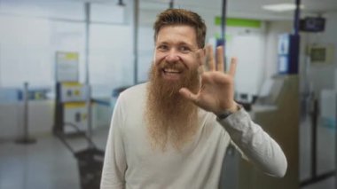 Genç sakallı adam geniş bir gülümseme ve meşgul havaalanı terminali kontrol alanında çıplak el sallayarak; dostça selamlama.
