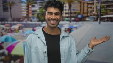 Gündüz vakti güneşli sahil gezintisinde gülümseyen İspanyol genç adam avuçlarını açık gösteriyor..