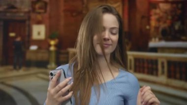 Kadın görünür bir yüzle gülümser ve kilisede ahşap sunakta akıllı telefonu tutar; dinginlik yansıması.