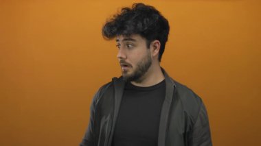 Sakallı genç İspanyol adam turuncu arka plana şaşırmış görünüyor.