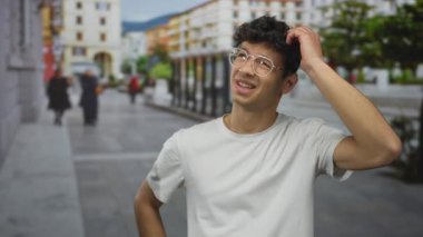 Genç Hispanik adam bulanık yayalar ve mağazalar arasında meşgul bir şehir caddesinde çene üzerine el koyar; tefekkür.