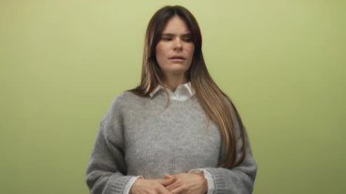 Sarı arka planda parmakları olan, gri bir kazak giyen, konsantrasyonunu gösteren ve izole bir ortamda odaklanan bir kadın..