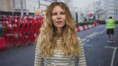Kadın saçı sokakları gözetliyor. Sarışın genç mankeni şehirdeki inşaat barikatında yakalamış. Mutlu poz..