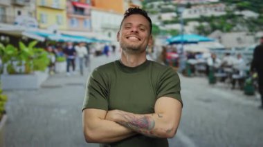 Şehir sokaklarında genç bir adam, canlı bir şehir arka planında mutluluk ve oyunculuğu ifade ederken dövmeleri ve kolları çaprazlanmış bir şekilde güvenle poz veriyor..