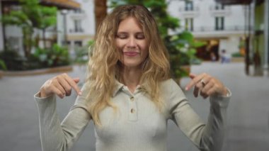 Kadın avludan elini kaldırdığında sarışın, genç bir gülümseme ve sıradan bir tişört giymiş bir şekilde elini kaldırır..