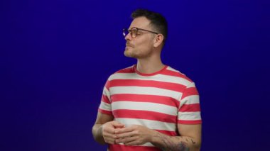 Mavi arka planda, çizgili gömlek ve gözlük takan genç adam, canlı kontrastı ve gündelik tarzı vurguluyor..