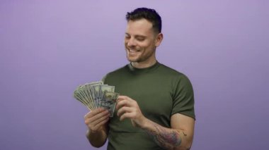 İspanyol asıllı genç bir adam Amerikan dolarlarını soyutlanmış mor arka planda tutuyor tatmin olmuş bir ifadeyle paraya bakıyor.