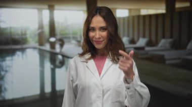 Kapalı kaplıcalarda havuz başında gülümseyen, beyaz bornoz giyen, jest yapan, baş parmağını kaldıran, dinlenme odasında dinlenen, pozitif bir ruh hali, sakin bir ortam sergileyen bir kadın..