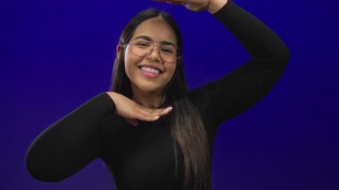 Kadın yüz çerçeveleme arka planda şık, genç Latin Latin kökenli izole edilmiş mavi duvar portresi yaratıyor. Bu portre etkileyici bir sırıtış ve kendine güvenen bakışları vurguluyor..