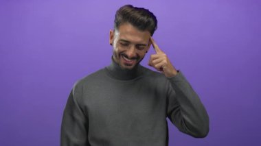 Gri balıkçı yaka ve sakallı İspanyol genç adam gülümsüyor ve stüdyoda parmak uçlarına kadar sırıtıyor..