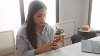 Yeni bir oturma odasında akıllı telefon kullanan genç bir kadın, sürpriz ve neşe gösteriyor, modern dekorasyon ve teknoloji ile çevrili, parlak bir dairede..