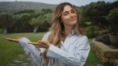 Genç sarışın kadın jestleri açık avuçlar ile bahçe yolunda zeytin ağaçları ve taş duvarlar ile sıralanmış; davet sükuneti.