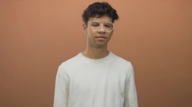 Adam beyaz süveter ve gözlük giyen turuncu stüdyo duvarına parmak işareti yapıyor; heyecan.