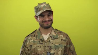 Askeri üniformalı genç adam stüdyoda gülümseyen ve avuçlarını silkeleyen; belirsizlik.
