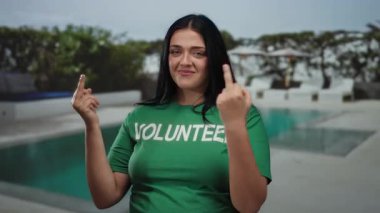 Yeşil gönüllü gömlekli bir kadın tatil köyündeki havuz başında beklenmedik bir şekilde samimi bir mizah ve kişilik gösterisi sunuyor..