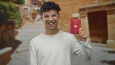 İspanyol adam, elinde Alman pasaportu tutarken gülümsüyor. Dar tarihi caddede. Gurur özgürlük yolculuğu..