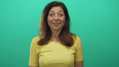 Stüdyoda iki eliyle yanaklarını tutan, ağzı açık ve gülümseyen bir kadın yeşil arka plana karşı. Sürpriz..