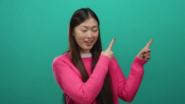 Pembe kazaklı kadın coşkuyla yeşil bir arkaplanı işaret ediyor. Heyecan ve olumlu duygular gösteriyor..