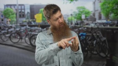 Kentsel caddedeki bisiklet kiralama parkında parmakla işaret eden adam, kot ceket görünür; konsantrasyon.