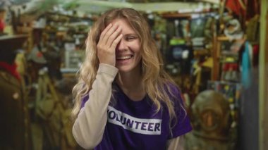 Kadın atölyede facepalm yapmak için elini kaldırıyor. Sarışın gönüllü, iç mekan zanaat ortamında kahkaha atıyor..